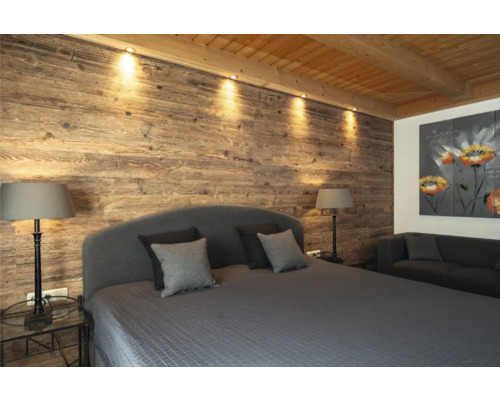 Schlafzimmer mit Holzwand, Bett, Nachttischen, Lampen und Sofa
