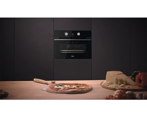Einbauofen der Marke Teka in einer dunklen Küchenzeile mit Pizza und Zutaten auf der Arbeitsfläche.