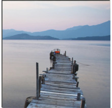 Ein langer Holzsteg führt ins ruhige Wasser eines Sees vor einer Bergkulisse.