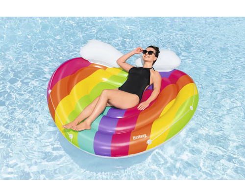 Frau entspannt auf einer regenbogenfarbenen, herzförmigen Luftmatratze im Wasser.