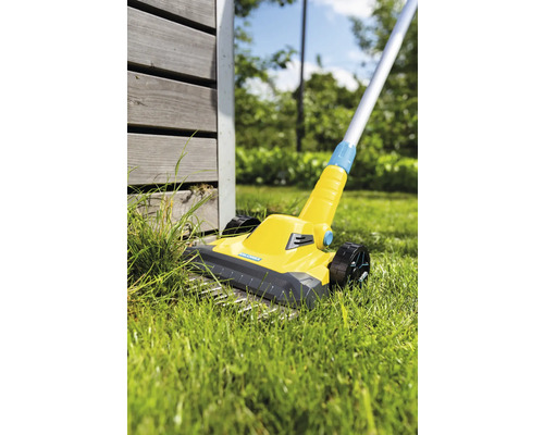 Gelber Vertikutierer im Einsatz auf Rasenfläche neben Holzwand.