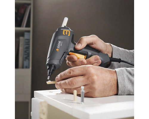 Eine Person benutzt eine Steinel Klebepistole zum Verkleben von Holzstücken auf einer weißen Oberfläche.