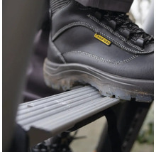 Ein Fuß in einem Sicherheitsschuh auf einer Trittstufe einer Leiter.