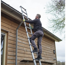 Eine Person steigt auf einer Teleskopleiter an einer Hauswand empor.