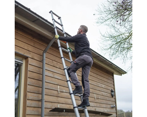 Eine Person steigt auf einer Teleskopleiter an einer Hauswand empor.