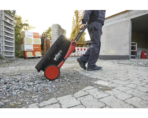 Handwerker zieht einen Werkzeugkoffer mit Rollen der Marke Wiha über einen gepflasterten Weg