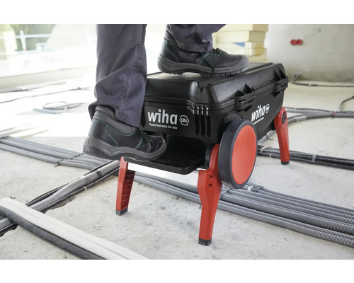 Person steht auf einem Wiha Werkzeugkoffer mit Rollen und ausklappbaren Beinen.