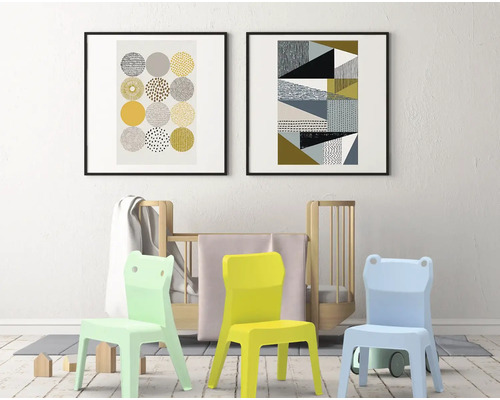 Zwei gerahmte abstrakte Kunstwerke hängen über einem Kinderbett und drei Kinderstühlen in einem Kinderzimmer.