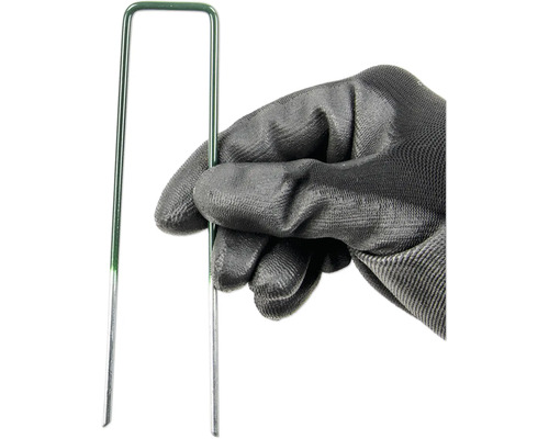 Une main avec un gant de jardin tient un clou à gazon vert.