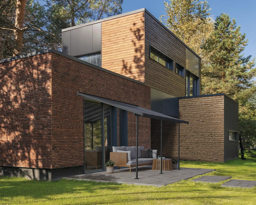 Modernes Haus mit Holzfassade, Backsteinmauer und Terrasse im Garten.