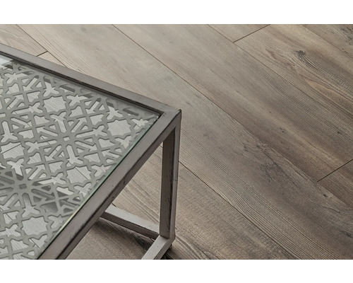 Detailansicht eines Tisches mit Glasplatte und dekorativem Muster, daneben ein Holzboden.