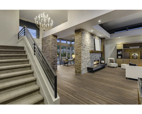 Innenaufnahme eines Wohnzimmers mit Treppe, Kamin, Holzboden und Beleuchtung