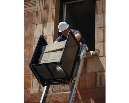 Bauarbeiter mit Schutzhelm transportiert Steine mit einer Steintransportkarre auf einer Leiter.