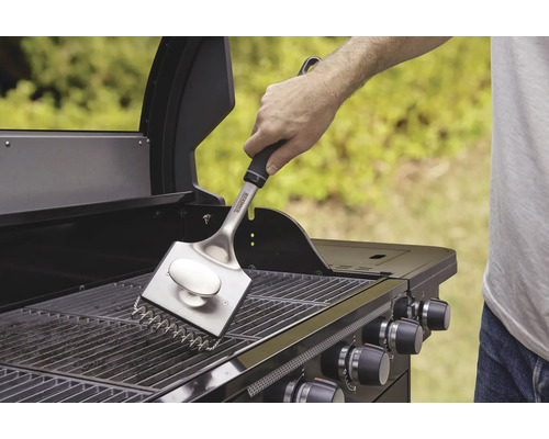 Une personne nettoie la grille du barbecue avec une brosse pour barbecue.