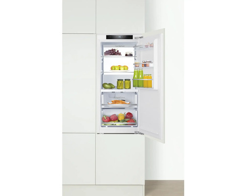 Réfrigérateur intégré avec porte ouverte, rempli de nourriture dans une armoire de cuisine.