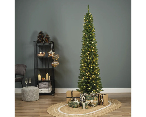 Sapin de Noël étroit et illuminé avec des cadeaux sur un tapis dans une pièce décorée.