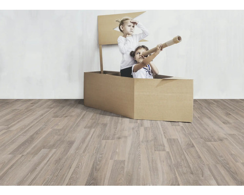 Deux enfants jouent dans un bateau en carton sur un plancher en bois.