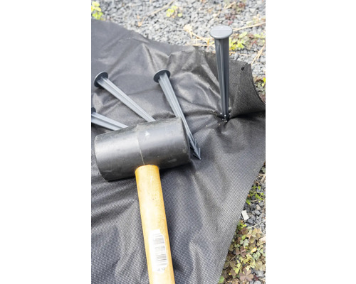 Gartenvlies wird mit einem Gummihammer und Erdankern fixiert.