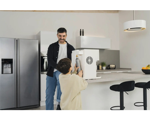 Un père et son fils remplacent une bouteille de CO2 dans un mousseur à eau dans une cuisine moderne