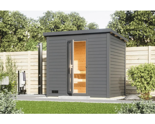 Chalet sauna Karibu Talos 3 sans poêle et porte en bois et verre isolant gris terre cuite Sauna de jardin moderne avec douche extérieure et clôture en bois en arrière-plan.