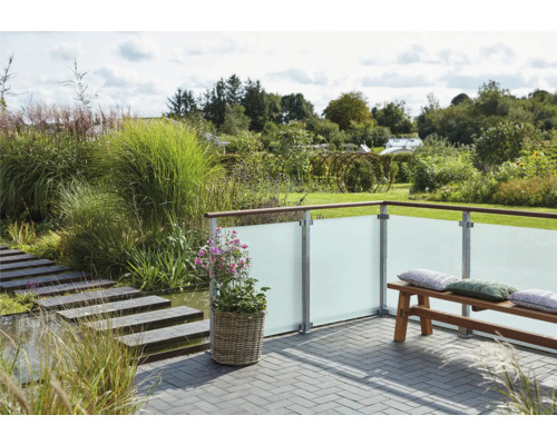 Terrasse avec paroi de protection visuelle en verre, banc et plantation dans un jardin.