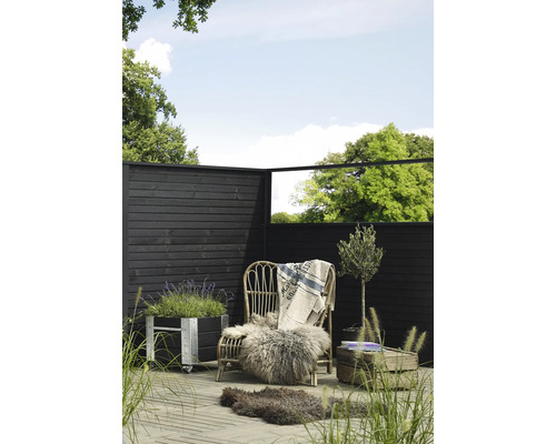 Scène de jardin avec clôture en bois, fauteuil en rotin avec fourrure et couverture, jardinière et olivier