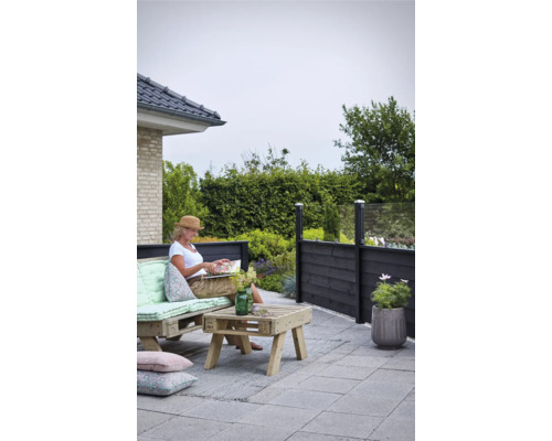 Scène de terrasse avec clôture de palissade, meubles en palettes et une femme lisant un livre