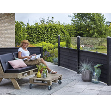 Scène de terrasse avec une femme assise sur un canapé en palettes, une table en palettes et un écran de confidentialité