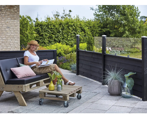 Scène de terrasse avec une femme assise sur un canapé en palettes, une table en palettes et un écran de confidentialité